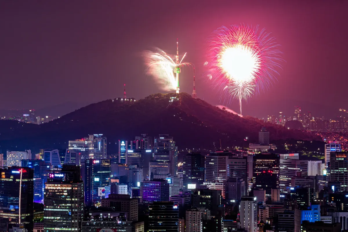 Vibrant fireworks illuminate the skyline of Seoul with Namsan Tower in view.