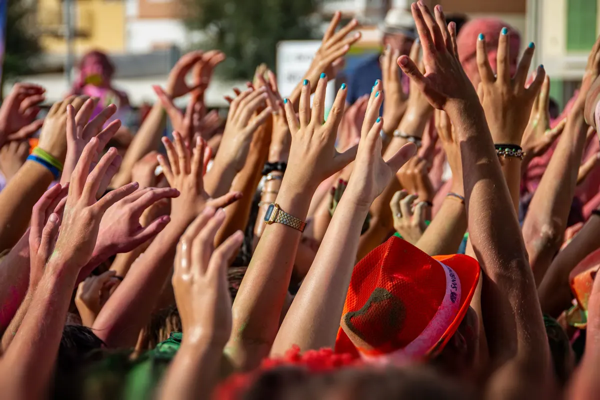 A vibrant scene of people with colorful hands raised at an outdoor festival.