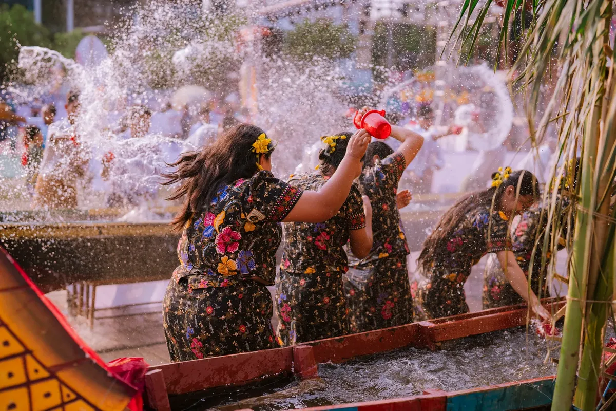 Colorful cultural water festival with women in traditional attire playfully splashing water.