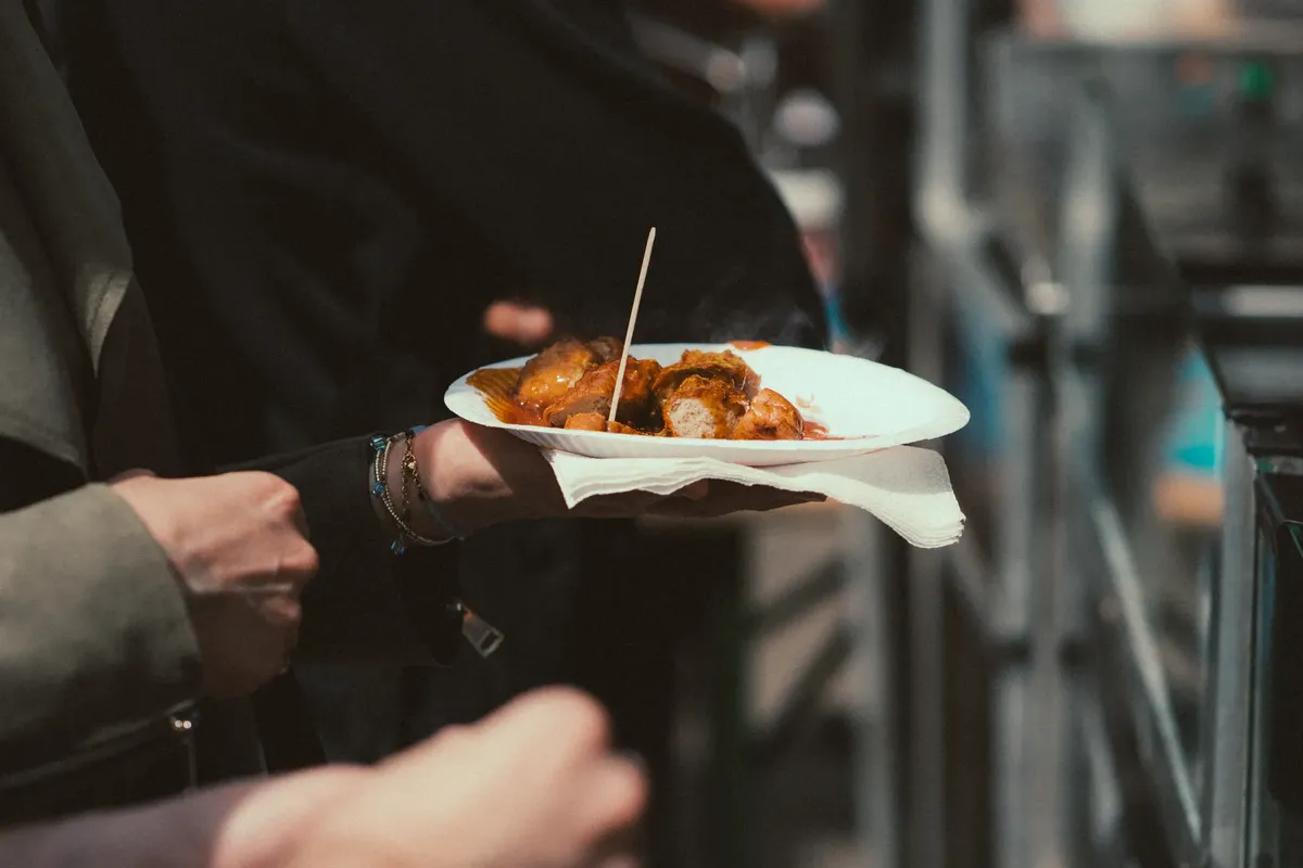 Person holding a plate of savory street food at an outdoor market.