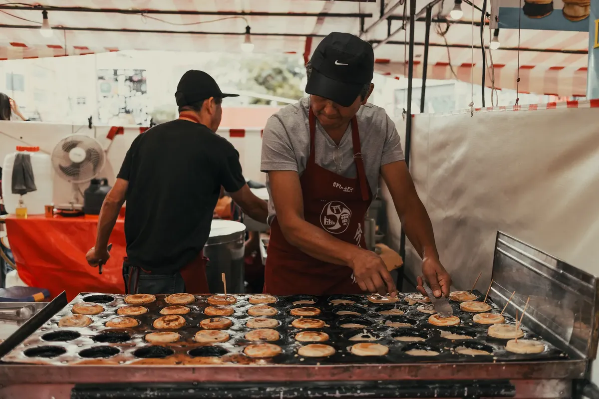 Asian street food vendor preparing snacks outdoors at a bustling market.