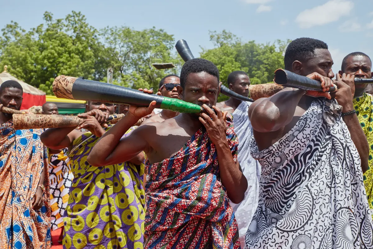 Men in traditional attire playing horns during an African cultural festival.