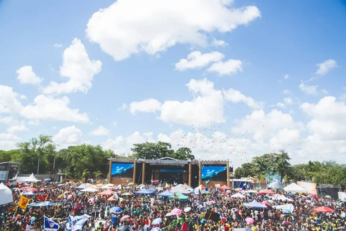 Lively outdoor festival with large crowd, vibrant umbrellas, and a clear sky in Santos Reis, Brazil.