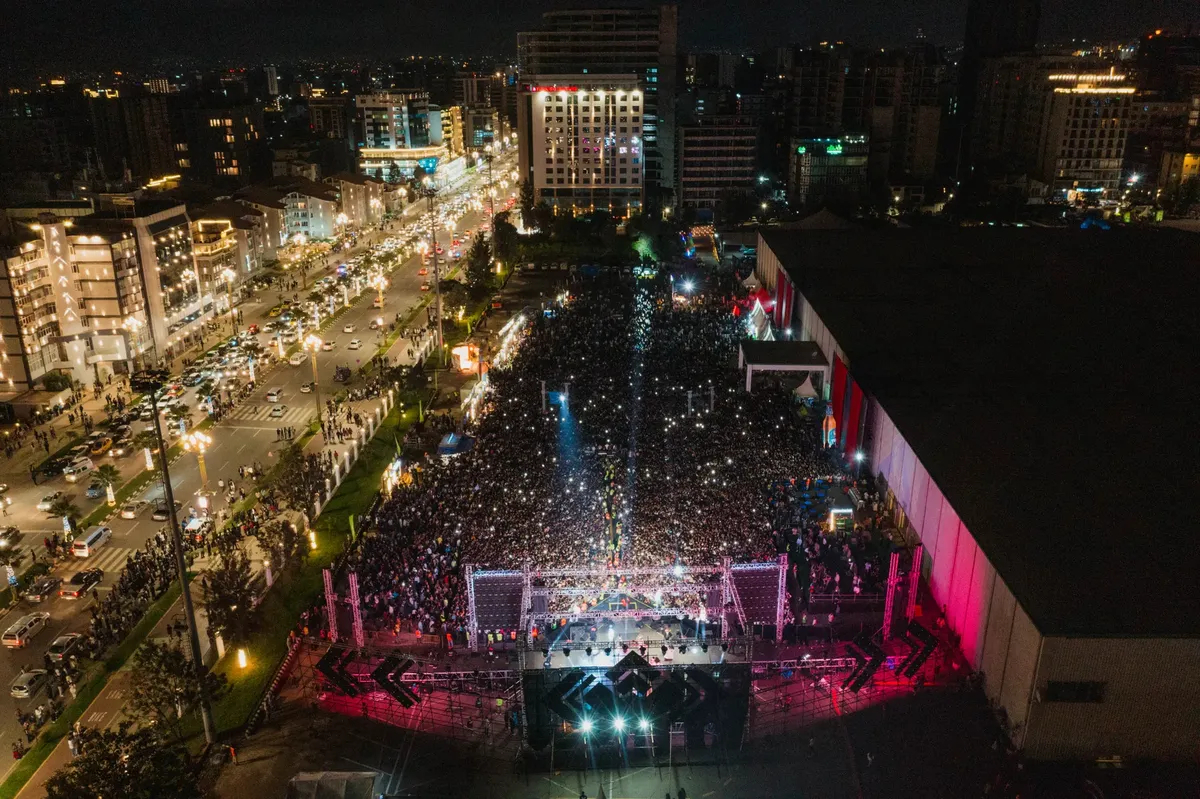 Vibrant aerial shot of a large crowd at a night city concert, illuminated by city lights.